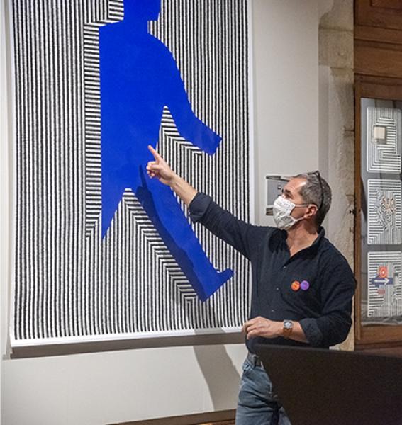 mediateur montrant du doigt une affiche représentant une silhouette bleue sur fond de lignes verticales noires et blanches