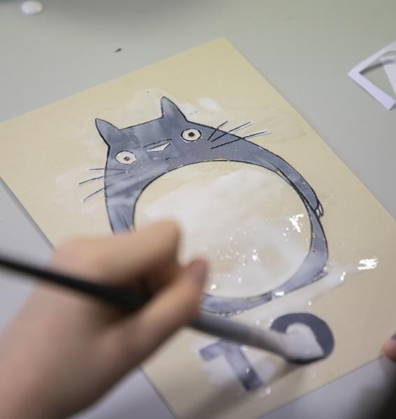 gros plan sur une main qui, au moyen d'un pinceau, peint une partie d'une image de Totoro