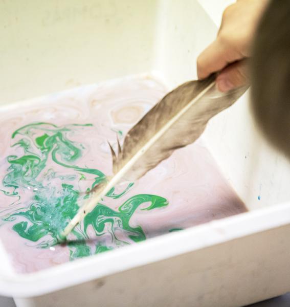 main touillant dans de l'eau encrée de différentes couleurs au moyen d'une plume