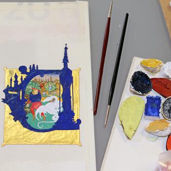 enluminure, pinceaux et peinture posés sur une table vue de haut