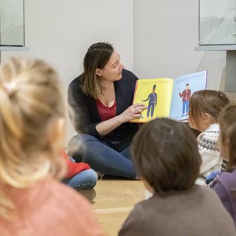 médiatrice en train de lire un livre illustré à des enfants assis par terre