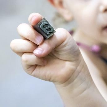 un enfant tient entre ses doigts un caractère mobile de typographie