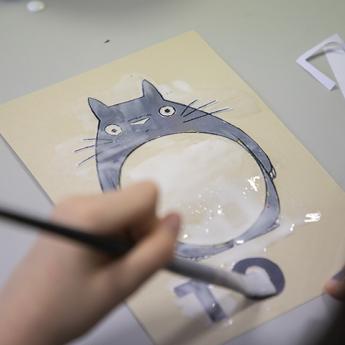 gros plan sur une main qui, au moyen d'un pinceau, peint une partie d'une image de Totoro