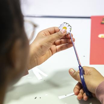 main qui tient une paire de ciseaux qui découpe une image de fleur sur papier