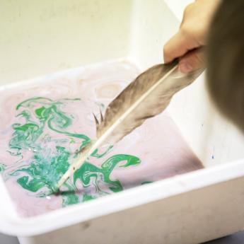 main touillant dans de l'eau encrée de différentes couleurs au moyen d'une plume