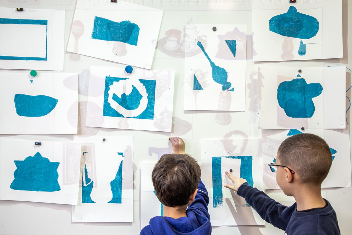 faire musée à l'école : des élèves devant un tableau rempli de sérigraphies réalisées par les enfants