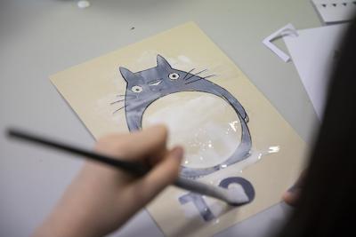 gros plan sur une main qui, au moyen d'un pinceau, peint une partie d'une image de Totoro