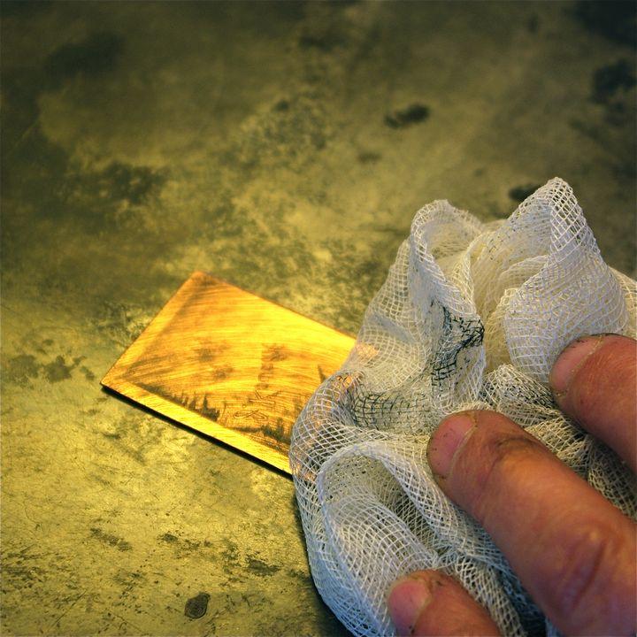 Main d'un graveur en train de nettoyer une plaque de métal gravée